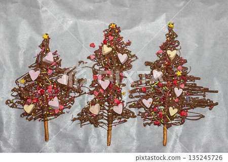 Three chocolate Christmas trees decorated with hearts sprinkles and colorful candy toppings Three chocolate Christmas trees decorated with hearts sprinkles and colorful candy toppings 135245726