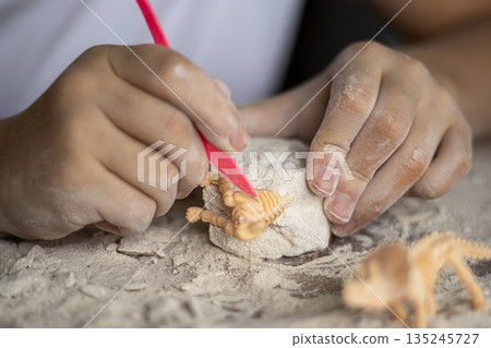 Child shaping dough with pink tool, sculpting a small orange dinosaur in a floury block 135245727