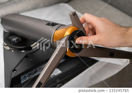 Person's hand carefully attaching a stylish monitor stand onto the back of a new computer screen, emphasizing assembly and user setup 135245785