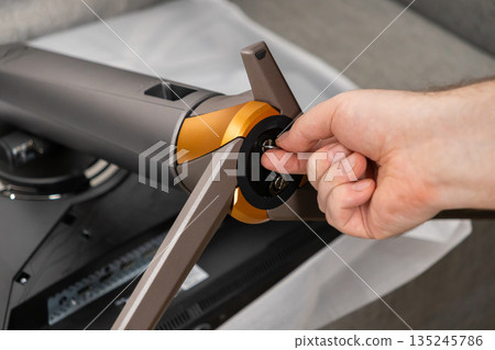 Close-up of a hand attaching a modern computer monitor stand with stylish grey and golden design, emphasizing efficient technology assembly and setup 135245786