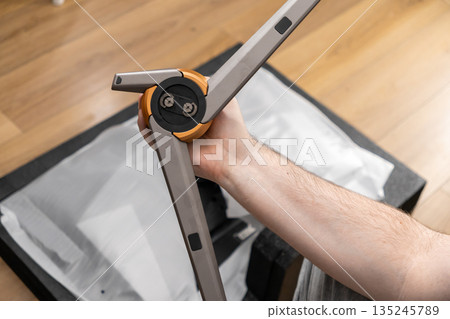 A person's hand holding a professional gray and orange tripod, highlighting its sturdy design and intricate joint for camera setup and content creation 135245789