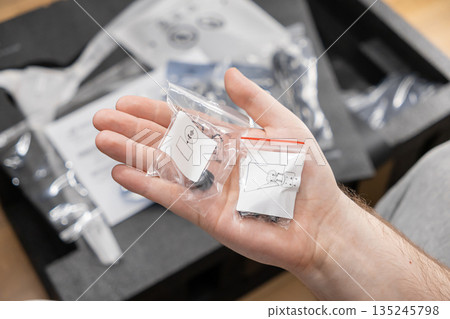 Person's hand holds two small clear bags with hardware and visual instructions, symbolizing product assembly, DIY project, and successful installation Person's hand holds two small clear bags with hardware and visual instructions, symbolizing product assembly, DIY project, and successful installation 135245798
