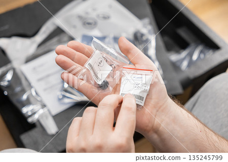 Person's hands holding two small plastic bags with assembly components and diagram labels, illustrating product setup, installation, and unboxing new items Person's hands holding two small plastic bags with assembly components and diagram labels, illustrating product setup, installation, and unboxing new items 135245799