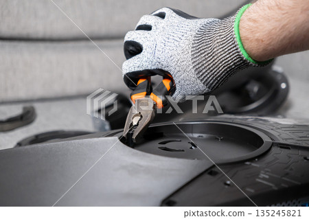 Skilled hand in protective glove uses pliers to repair complex electronic device components, emphasizing technical maintenance and careful assembly work Skilled hand in protective glove uses pliers to repair complex electronic device components, emphasizing technical maintenance and careful assembly work 135245821