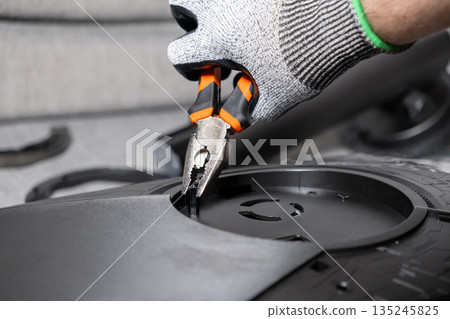 Gloved hand expertly operates orange-handled pliers to precisely fit a small electronic part onto a black device, representing detailed technical assembly and repair Gloved hand expertly operates orange-handled pliers to precisely fit a small electronic part onto a black device, representing detailed technical assembly and repair 135245825