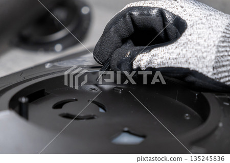 Professionals gloved hand precisely inserting a small screw standoff into a complex black electronic component, showcasing meticulous assembly and technical service 135245836
