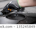 Expert's gloved hand carefully operates a small ratchet wrench, fastening a screw on black electronic equipment, signifying precise technical repair and assembly 135245849