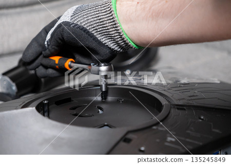 Expert's gloved hand carefully operates a small ratchet wrench, fastening a screw on black electronic equipment, signifying precise technical repair and assembly Expert's gloved hand carefully operates a small ratchet wrench, fastening a screw on black electronic equipment, signifying precise technical repair and assembly 135245849