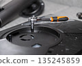 Close-up of a silver ratchet wrench with orange and black handle tightening a screw on a complex disassembled electronic device, highlighting precision repair work 135245859