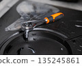 Chrome ratchet wrench with an ergonomic orange handle fastening a hex screw on a dark electronics base, showcasing precision technical repair and equipment assembly 135245861