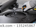 Skilled technician's gloved hand uses a precise ratchet wrench to secure a vital screw within a disassembled computer monitor, symbolizing meticulous hardware repair and upgrade service 135245867