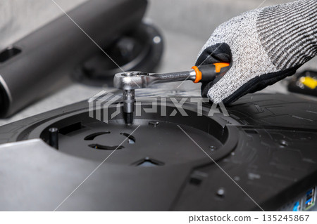 Skilled technician's gloved hand uses a precise ratchet wrench to secure a vital screw within a disassembled computer monitor, symbolizing meticulous hardware repair and upgrade service 135245867