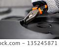 Expert hand in work glove uses orange pliers to install a small black hex standoff, symbolizing meticulous electronic assembly and technical repair 135245871