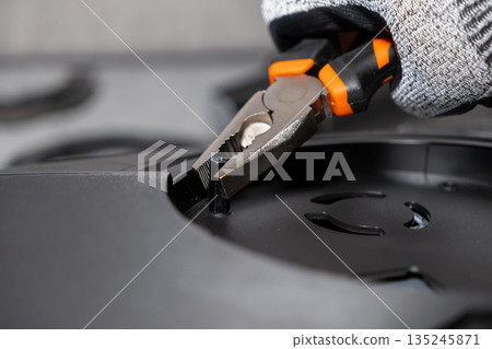 Expert hand in work glove uses orange pliers to install a small black hex standoff, symbolizing meticulous electronic assembly and technical repair Expert hand in work glove uses orange pliers to install a small black hex standoff, symbolizing meticulous electronic assembly and technical repair 135245871