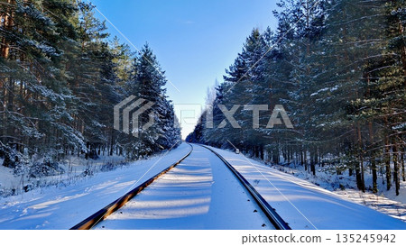 Snow-Covered Railway Tracks Through Winter Forest. Curved railroad tracks covered in fresh snow winding through dense pine forest under clear blue sky at sunrise. Winter travel, adventure and serene n Snow-Covered Railway Tracks Through Winter Forest. Curved railroad tracks covered in fresh snow winding through dense pine forest under clear blue sky at sunrise. Winter travel, adventure and serene n 135245942