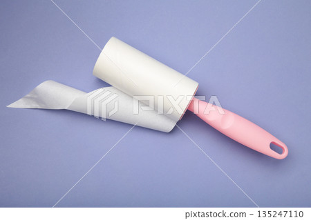 Cloth fabrics cleaner lint roller brush with paper roll on purple background. Sticky roller, pet cat dog fur dust hair remover Cloth fabrics cleaner lint roller brush with paper roll on purple background. Sticky roller, pet cat dog fur dust hair remover 135247110