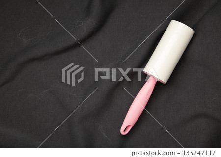 Lint roller resting on a dark suit jacket to remove pet animal hair. Lint roller resting on a dark suit jacket to remove pet animal hair. 135247112
