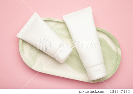 White plastic cosmetic tubes on plate on pink background. Space for text 135247123