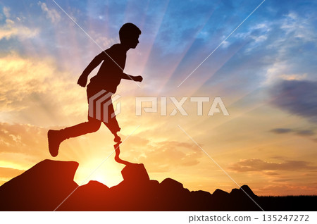 Silhouette of disabled boy with prosthetic leg running on rocks against stunning sunset Silhouette of disabled boy with prosthetic leg running on rocks against stunning sunset 135247272