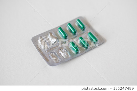 Semi-empty metal blister pack with yellow capsules isolated on white background. Metal blister for capsules 135247499