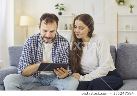 Couple browsing on tablet at home, searching options together on cozy sofa 135247594