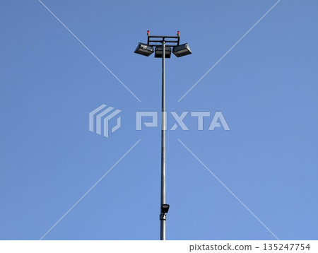minimalist floodlight pole under bright sky, single tall floodlight mast with lamp cluster 135247754