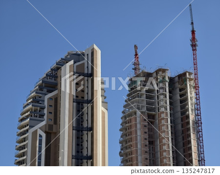 highrise juxtaposition with twin cranes, cityscape showing retrofit options and contrasting facades 135247817
