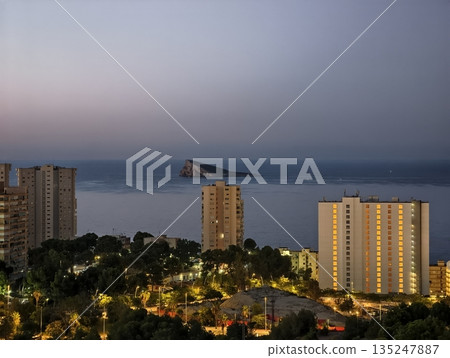 peaceful urban harbor with evening glow, quiet seaside skyline illuminated under gentle evening mist 135247887