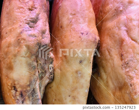 Aged cured ham with mold patches in warm amber lighting 135247923