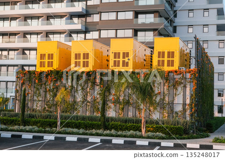 Yellow industrial generators installed on a landscaped platform in a modern residential complex, showing urban infrastructure Yellow industrial generators installed on a landscaped platform in a modern residential complex, showing urban infrastructure 135248017