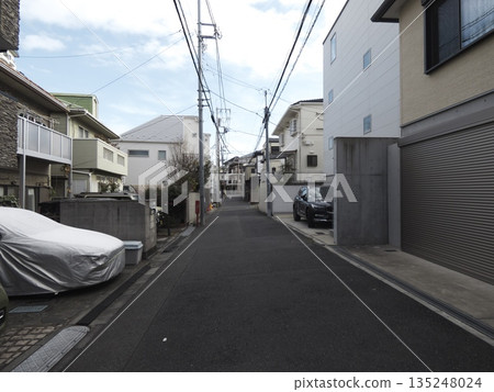 A quiet residential street stretches out beneath the clear winter sky. Telephone poles and power lines crisscross the street, creating a tranquil, everyday Japanese scene. A quiet residential street stretches out beneath the clear winter sky. Telephone poles and power lines crisscross the street, creating a tranquil, everyday Japanese scene. 135248024