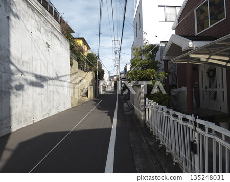A residential alleyway where winter sunlight and shadows intersect. A quiet streetscape lined with high concrete retaining walls. 135248031