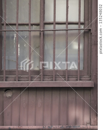 廢棄房屋的窗戶和鏽跡斑斑的鐵欄桿暴露在時間的侵蝕下。這些古老的日本房屋殘骸已被遺棄,正在悄悄腐朽。 廢棄房屋的窗戶和鏽跡斑斑的鐵欄桿暴露在時間的侵蝕下。這些古老的日本房屋殘骸已被遺棄,正在悄悄腐朽。 135248032
