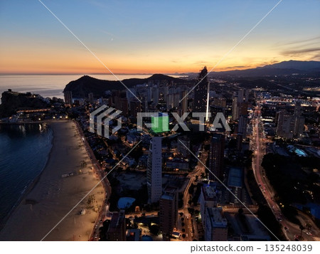 vibrant night beachscape scene, lively shoreline silhouette with illuminated promenade and sandy bay 135248039