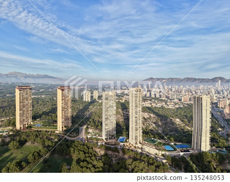urban area meets mountain range, city sprawls towards towering mountains beneath clear bright sky 135248053