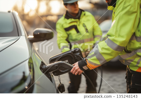 Electric Vehicle Charging Station Workers in Safety Gear Powering a Car Electric Vehicle Charging Station Workers in Safety Gear Powering a Car 135248143