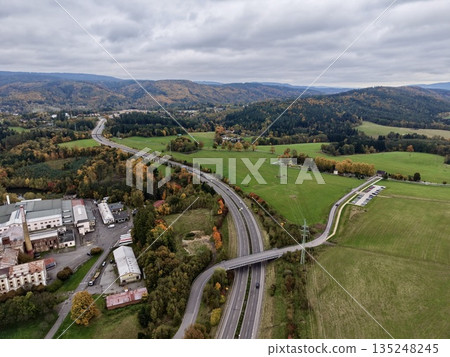 Twin Lane Road Surrounded By Vegetation, Roadway Flanked By Greenery And Distant Tree Lines Under Cloudy Sky Twin Lane Road Surrounded By Vegetation, Roadway Flanked By Greenery And Distant Tree Lines Under Cloudy Sky 135248245