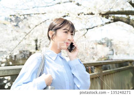 A woman using a smartphone under a cherry tree A woman using a smartphone under a cherry tree 135248271