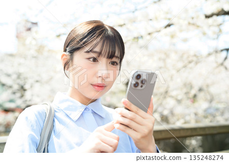A woman using a smartphone under a cherry tree 135248274