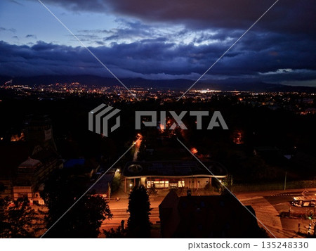 Suburban Evening Scene, Calm Suburban Street At Dusk With Distant City Shimmer And Glowing Storefronts Suburban Evening Scene, Calm Suburban Street At Dusk With Distant City Shimmer And Glowing Storefronts 135248330