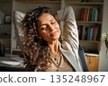 Relaxed woman enjoying peaceful moment at home office with sunlight streaming in a library bookcase background 135248967
