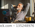 Relaxed mature man enjoying sunlit break at home office, feeling peaceful and calm after work 135248976