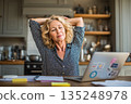 Relaxed Woman Stretching at Home Office Desk near Laptop, enjoying a break from work 135248978