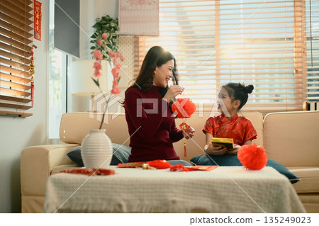 Mother and daughter sit together decorating red lanterns ornaments for Chinese New Year, sharing a joyful family moment 135249023
