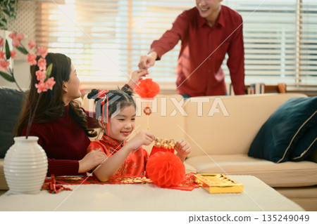 Happy family decorating home for Chinese New Year as father hands a red ornament to mother and daughter Happy family decorating home for Chinese New Year as father hands a red ornament to mother and daughter 135249049