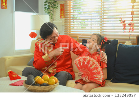 Grandfather gently talks and jokes with his granddaughter while sitting together during a warm Chinese New Year Grandfather gently talks and jokes with his granddaughter while sitting together during a warm Chinese New Year 135249057