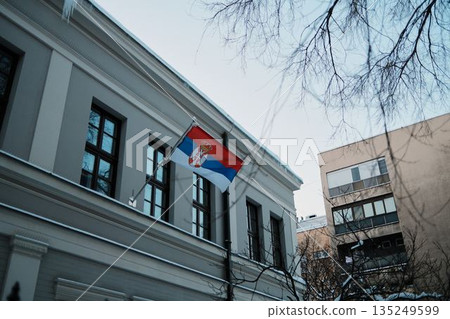 Serbian national flag displayed on historic government building during winter day. Symbol of national identity, state authority, and architectural heritage 135249599