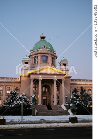 Grand historic building with green dome illuminated during winter evening. The image highlights monumental architecture, cultural heritage, and seasonal city scenery 135249602
