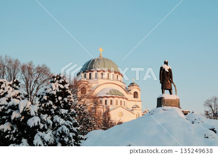 Orthodox St Sava church in Belgrade and historic monument stand covered with snow under clear winter sky. The scene reflects cultural heritage, faith, and winter atmosphere in the city 135249638