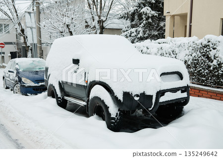 SUV stands parked on a city street completely covered with heavy snow. The image represents extreme winter weather and its effect on urban transportation SUV stands parked on a city street completely covered with heavy snow. The image represents extreme winter weather and its effect on urban transportation 135249642